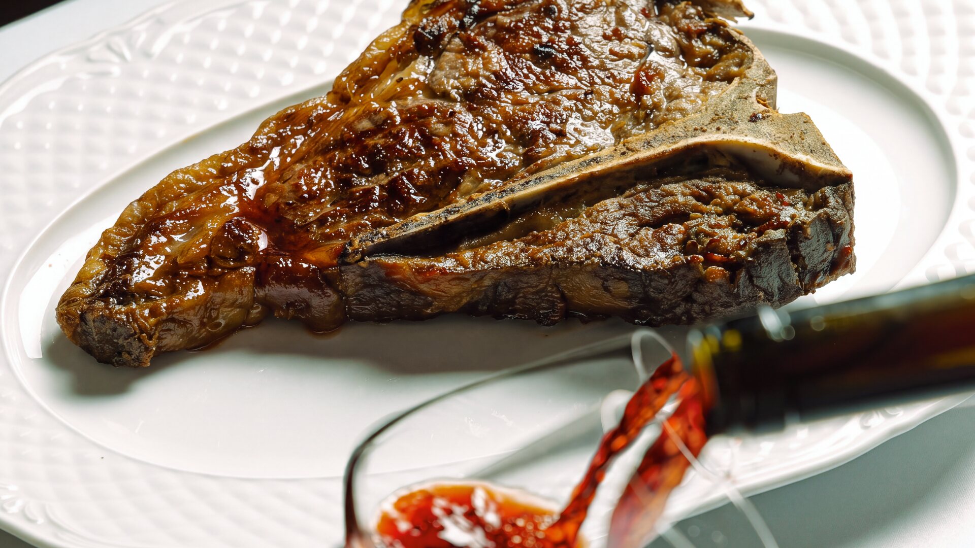 Bistecca alla Fiorentina su un piatto bianco mentre si versa il vino rosso