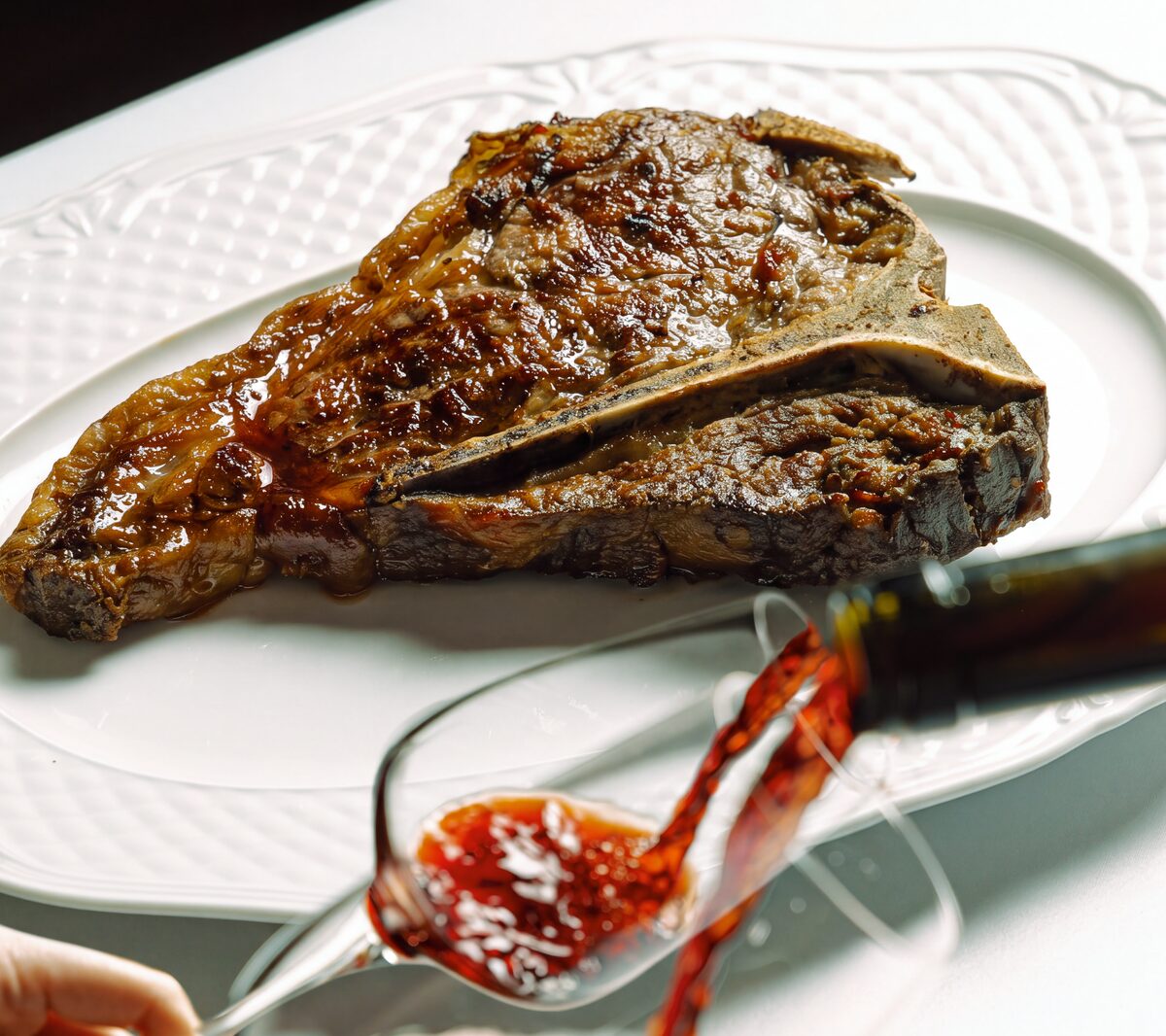 Bistecca alla Fiorentina on a white platter as red wine is poured